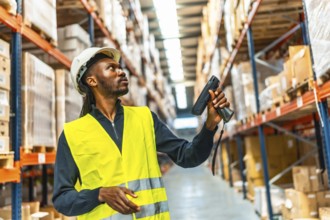 Side view of an african worker scanning package with bar code reader in a distribution warehouse