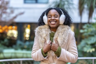 Happy young woman wearing cozy earmuffs and a stylish winter coat, smiling brightly while enjoying