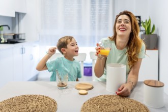 Mother and boy laughing while eating breakfast before going to school at home