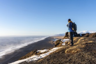 A tourist man at the viewpoint of Dyrholaey beach in the cold winter with snow in Iceland