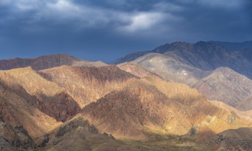 Red and orange mountains in atmospheric light, dramatic cloudy sky, mountain landscape near