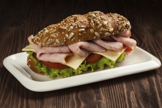Ham sandwich with lettuce, cheese, tomato on plate on wooden table