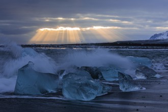 Waves breaking on icebergs on the black beach of Breidamerkursandur, sunset, near Jökullsarlon,