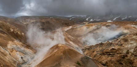 Steaming streams between colourful rhyolite mountains with snowfields, Hveradalir geothermal area,