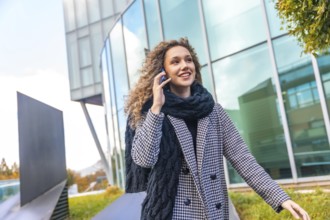 Portrait of a cute woman in elegant warm clothes using phone in the city