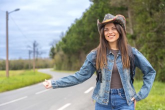 Woman in denim and cowboy hat hitchhiking in a rural road