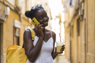 Young african woman talking with the mobile and drinking milkshake stranding on the street