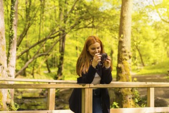 Woman photographer with a black jacket enjoying in an autumn park, taking pictures on a wooden