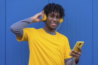 African boy listening to music with headphones next to a blue wall