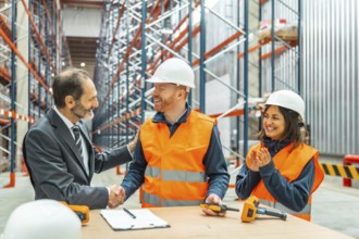 Manager shaking hands with a warehouse worker after closing a deal, his colleagues clapping hands,