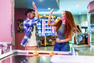 Two friends giving high five while enjoying a game of air hockey in a vibrant entertainment center,