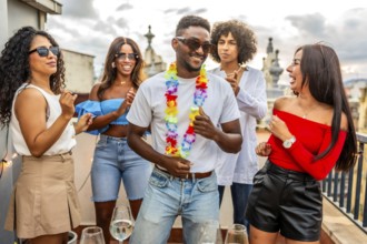 Happy latin man with Hawaiian necklace dancing with friends in outdoor rooftop party
