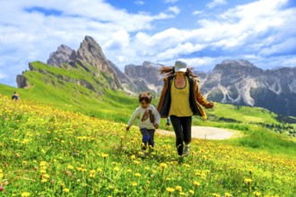 Mother and son running through a field of wildflowers in the italian dolomites mountains, enjoying