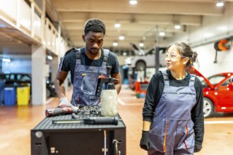 Two auto mechanics, a man and a woman, stand beside a workbench, reviewing tools and discussing car