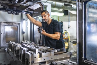Serious male caucasian engineer inspecting a milling machine in an innovative metal cnc factory