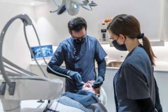 Dentist wearing magnifying glasses and face mask performing a dental procedure on a senior female