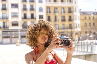 Beauty brunette woman with curly hair taking photos visiting a city in the summer