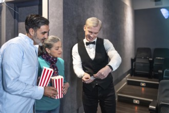 Couple entering a movie theater, holding popcorn buckets while the usher checks their tickets,