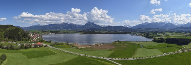 Expansive landscape with a view of Lake Hopfensee and mountains, surrounded by green meadows and a