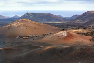Orange-coloured coach with tourists drives through the fire mountains of Timanfaya National Park,