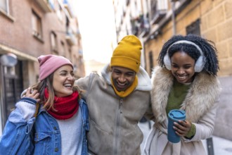 Three cheerful young multi ethnic friends are enjoying a winter day together, walking arm in arm
