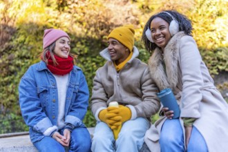 Group of young multi ethnic friends wearing winter clothes, sitting outdoors in the city and