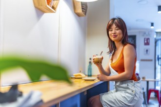 Portrait with copy space of a smiling asian youthful woman drinking coffee in a cafeteria