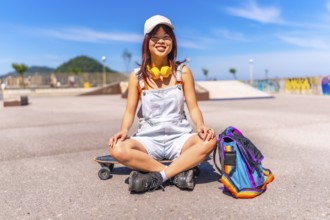 Asian woman sitting on skateboard smiling at camera in a public park