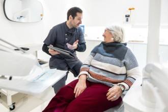 Dentist is explaining something on a tablet to a senior female patient during a consultation in a