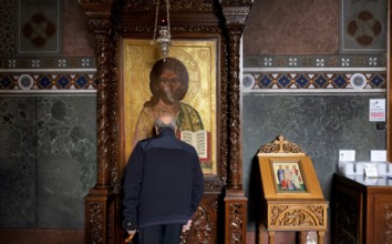 Elderly man praying in front of an image of a saint, from behind, interior view of Hagia Sofia