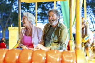 Happy caucasian senior couple enjoying a ride with carousel at night in the city