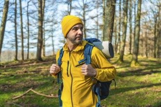 Male hiker in a bright yellow jacket and blue backpack walking through a lush forest, soaking up