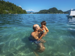 Father and son having fun swimming in the clear waters of lake bled, surrounded by the beauty of