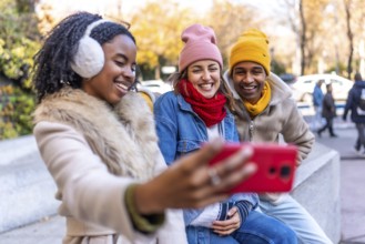 Three happy multi ethnic friends enjoying the outdoors, taking a cheerful selfie in a winter city