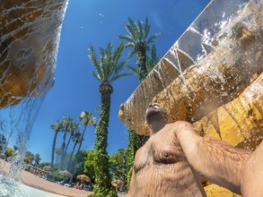 Man refreshing under a waterfall in a water park during summer vacation, enjoying the cool water