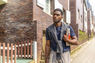 Young african entrepreneur walking the street with reusable coffee thermos and laptop