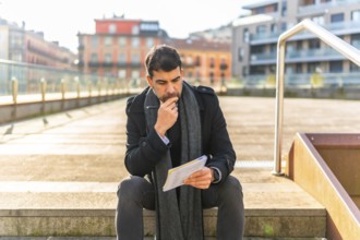 Casual businessman writing notes sitting with pensive expression in a city square in winter