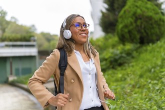 Portrait of a happy latin businesswoman listening to music commuting in the city walking down a