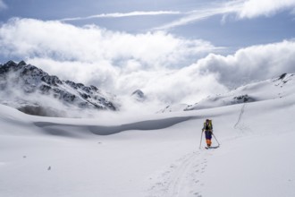 Atmospheric clouds in a wintry mountain landscape, ski tourer on the ascent to Porta d'Es-cha,