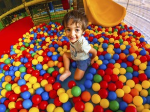 A young boy is playing in a ball pit, surrounded by a colorful sea of balls. He is smiling and he