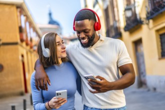 Happy young multi-ethnic couple using mobile and listening to music walking together in the city
