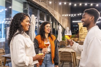 Multi-ethnic friends talking while drinking beer at night in an elegant roof terrace of a bar