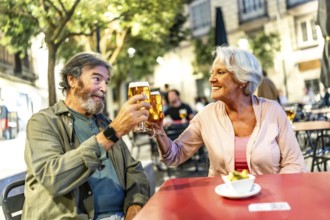 Happy relaxed senior couple toasting with beer in sidewalk cafeteria at night