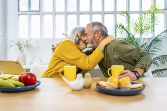 Senior woman whispering at the ear of her husband enjoying breakfast together at home
