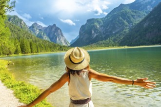 Woman wearing straw hat with open arms enjoying the pristine waters of lake dobbiaco and the