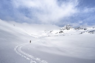 Ski tourers ascending through a picturesque snow-covered mountain landscape with peaks, ascent to