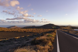 Road leads through hilly volcanic landscape, Famara Mountains, evening sky, Cumulus, Los Valles,