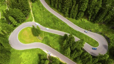 Aerial view of cars driving on a winding mountain road surrounded by lush green forest in the