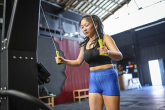 Low angle view of a strong Chinese young woman pulling weights using lat rowing machine in the gym