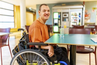 Three quarter length photo of a smiling caucasian man with disability sitting drinking water in the